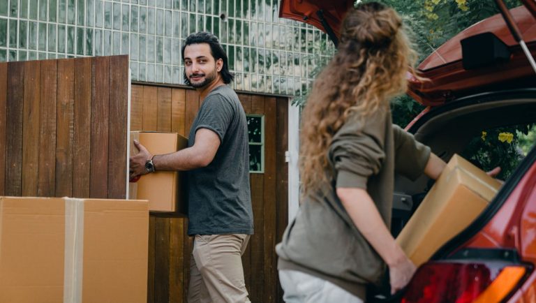 Couple loading cardboard boxes into the trunk of a car outside a house